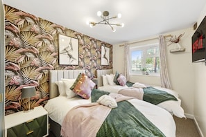 Une chambre avec deux lits, une grande fenêtre, un téléviseur fixé au mur et un papier peint orné de motifs de feuilles tropicales.