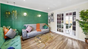 A living room with a green accent wall, a grey sofa with orange and green cushions, and two glass coffee tables. - Luxury House in Bristol with Hot Tub - Sleeps 10 (Bristol)