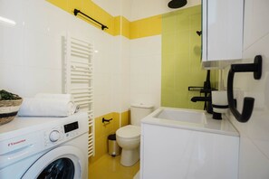 A compact bathroom with a washing machine, toilet, and sink.