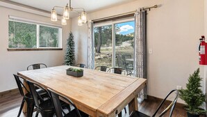 En matplats med ett träbord, svarta stolar och en kristallkrona. Det finns ett fönster med utsikt över träd och en dörr som leder ut.