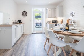 Eine moderne Küche mit weißen Schränken, einer Holzausziehtheke und einem Essbereich mit weißen Stühlen und einem Holztisch.