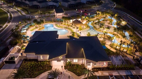Une vue aérienne d’un complexe hôtelier doté d’une piscine, de palmiers et d’un bâtiment bien éclairé comprenant de nombreuses chambres.