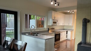 A modern kitchen with white cabinetry, a central island, stainless steel appliances, and a black stove. - 2 bedroom Oceanfront  - Billing spit (Sooke)