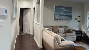 A spacious living room with a beige sectional sofa, a painting on the wall, and a modern floor lamp. - 2 bedroom Oceanfront  - Billing spit (Sooke)