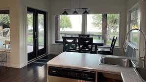 A modern kitchen with a dishwasher, a sink, and a dining area with chairs and a table. - 2 bedroom Oceanfront  - Billing spit (Sooke)