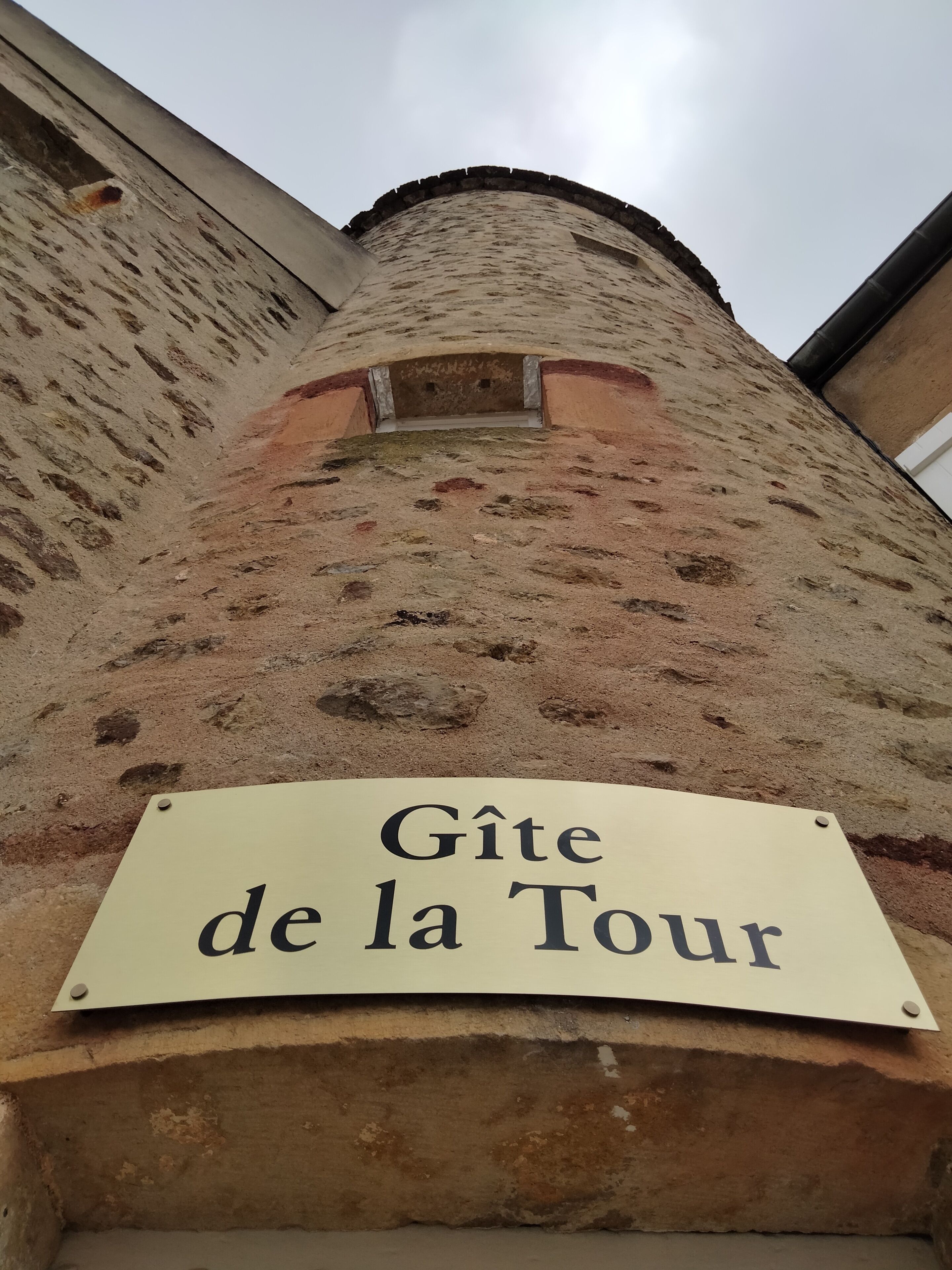 A sign reading "Gîte de la Tour" mounted on a stone wall.