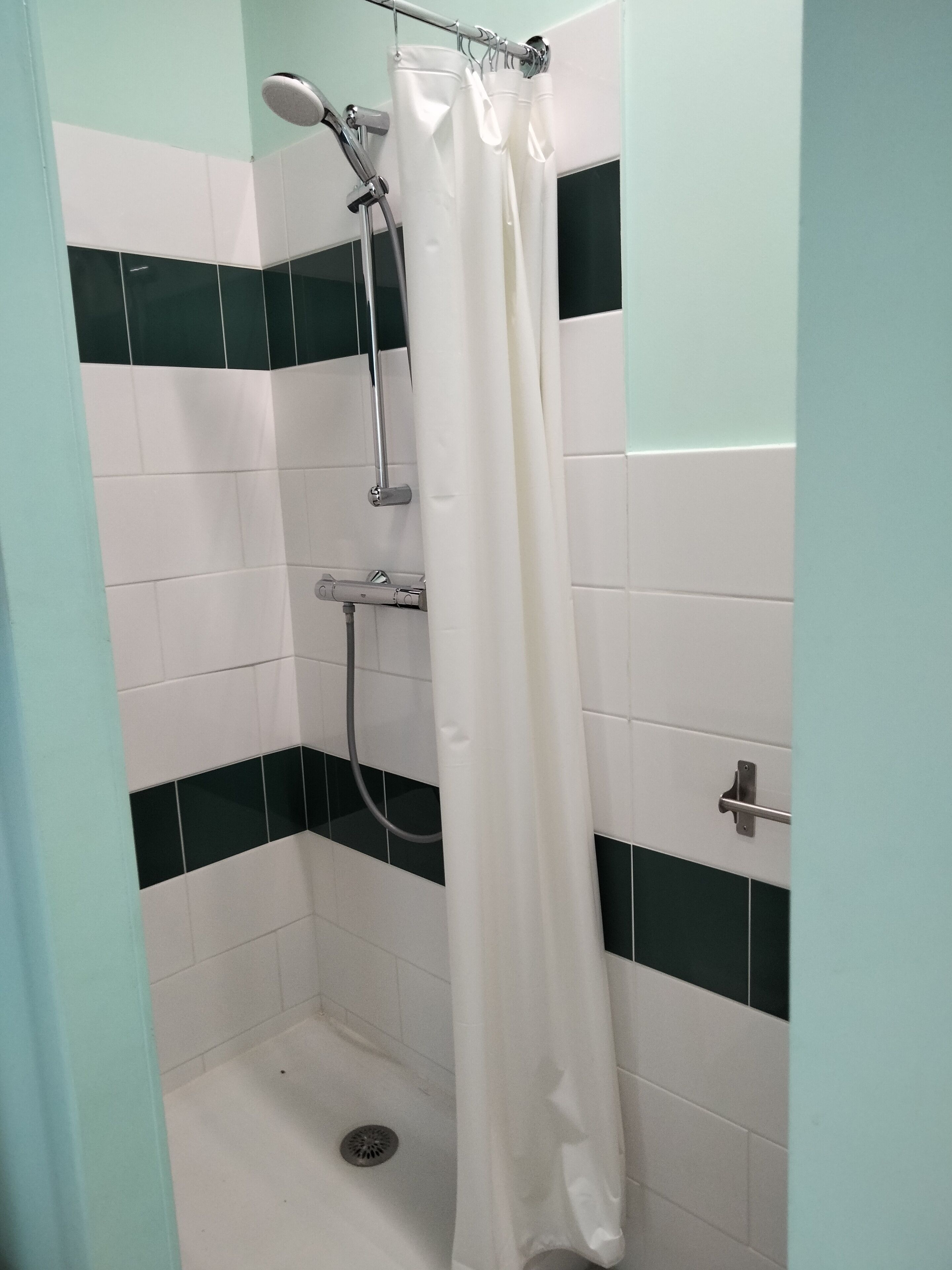 Une douche avec un rideau blanc, une douchette à main et un robinet fixé au mur.