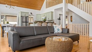 En moderne stue med en grå sofa, et vævet sofabord og en trappe, der fører til en etage ovenover.