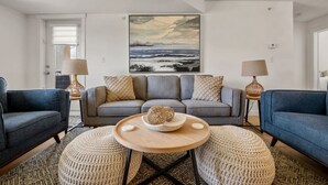 A living room with a grey sofa, two armchairs, a round coffee table, and a painting above the sofa. - Tranquil Waterside | Pool & Hot Tub | Renovated (Invermere)