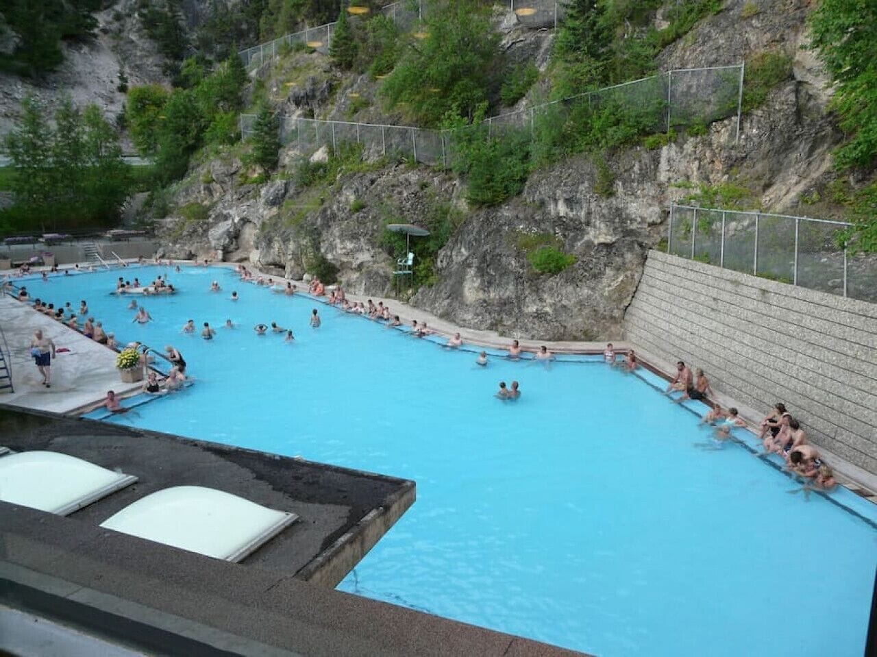 Una amplia piscina exterior con múltiples carriles, rodeada por un risco y vegetación.