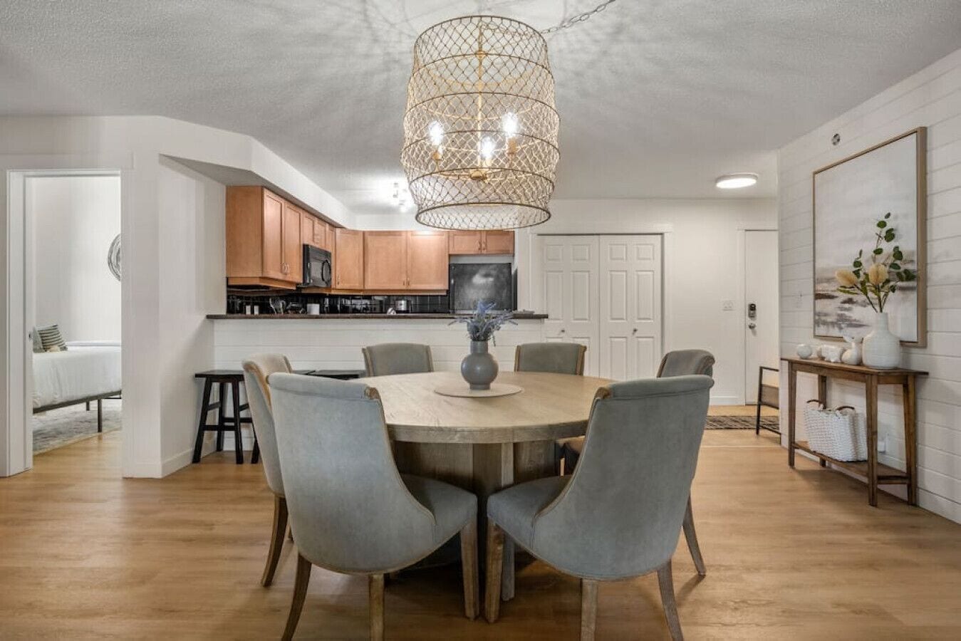 Un coin repas avec une table ronde, des chaises à revêtement gris, un luminaire suspendu et une cuisine en arrière-plan.