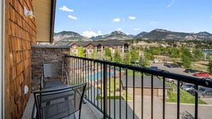 A balcony with a view of a mountain range, a pool, and a parking area. - Tranquil Waterside | Pool & Hot Tub | Renovated (Invermere)