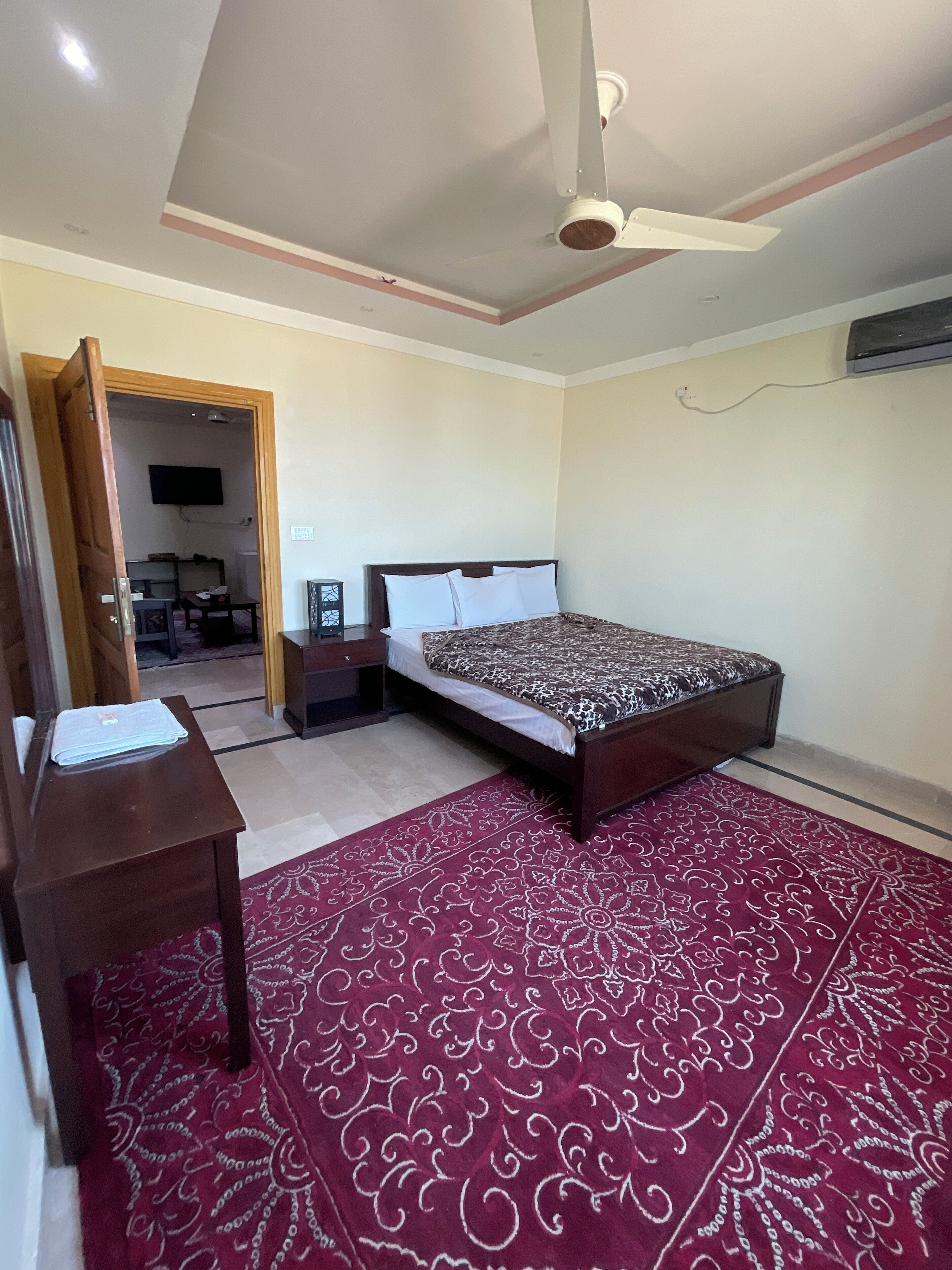 A bedroom with a bed, a desk, a chair, a ceiling fan, and a TV.