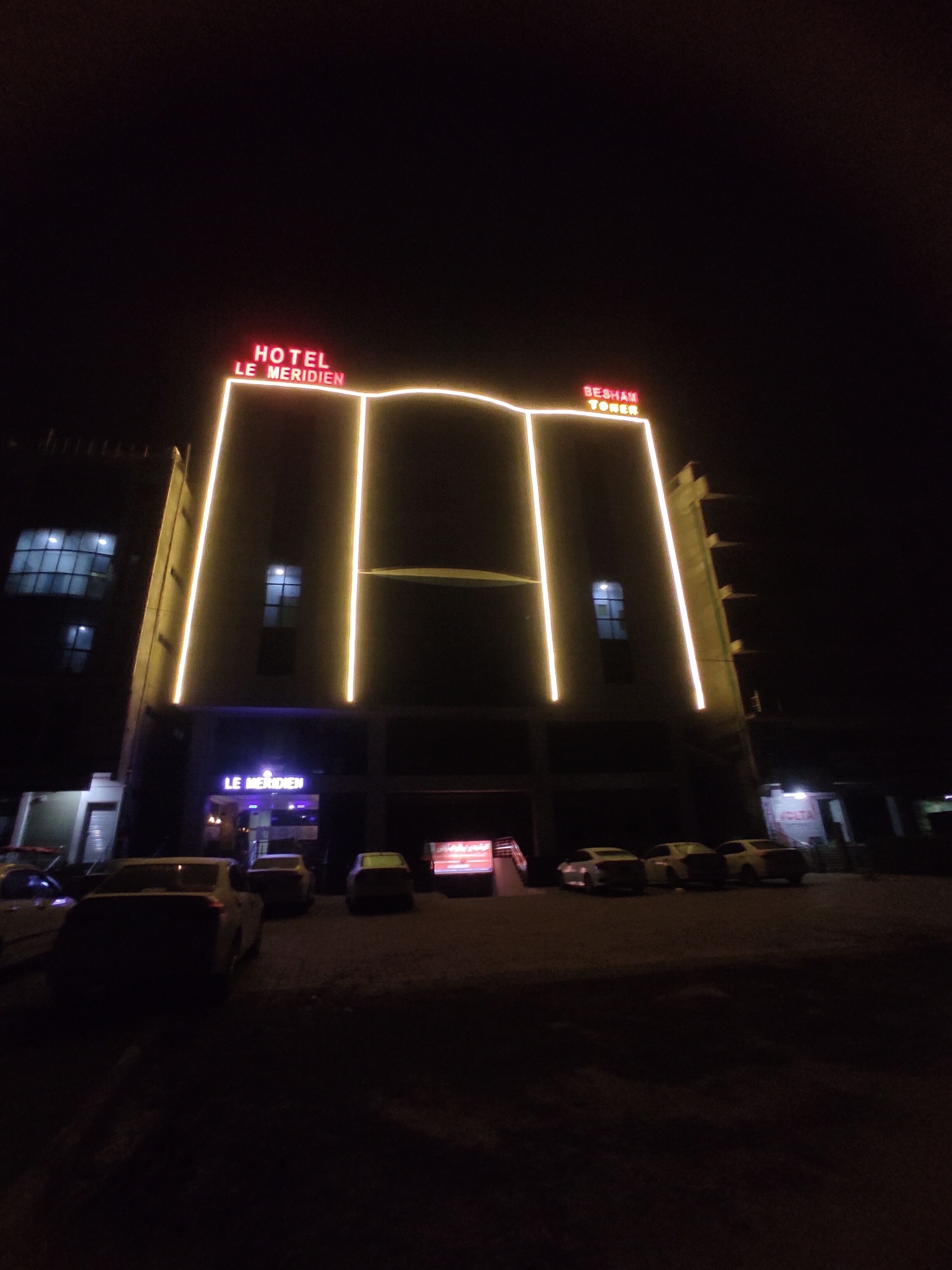 Un hôtel dont l’enseigne lumineuse affiche les inscriptions « HÔTEL LE MERIDIEN » et « HÔTEL BESHAMS ».