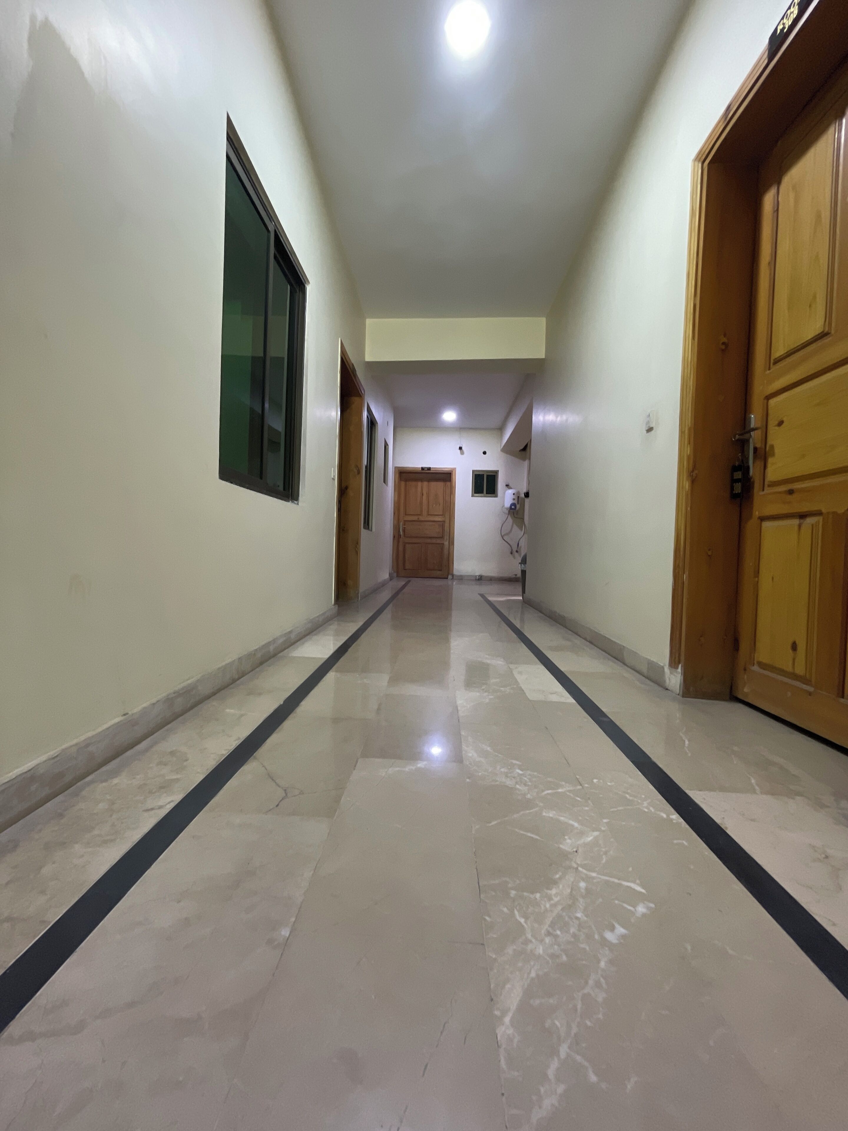 A hallway with a tiled floor, wooden doors, and a ceiling light.