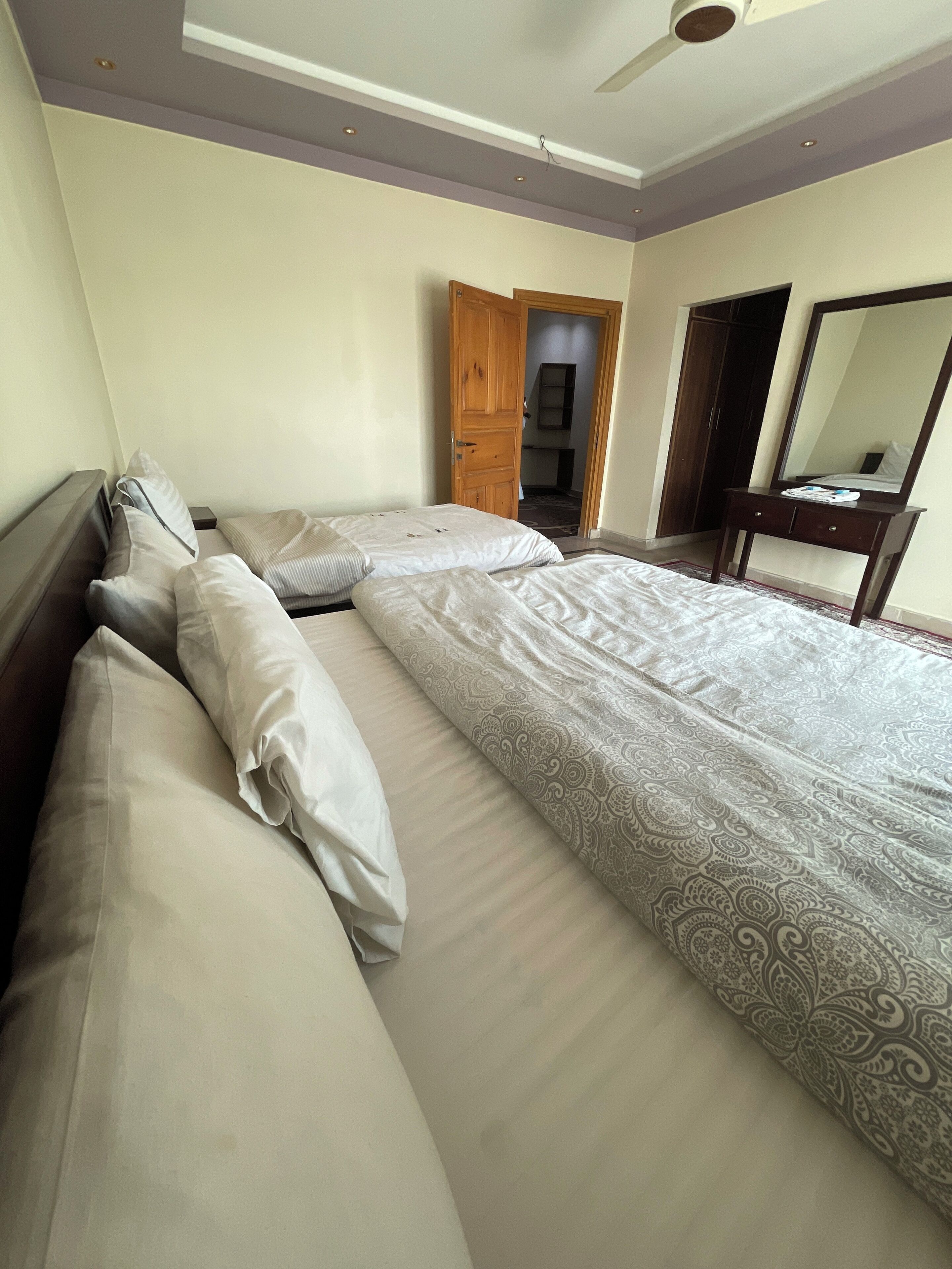 A hotel room with two beds, a wooden wardrobe, a mirror, and a ceiling fan.