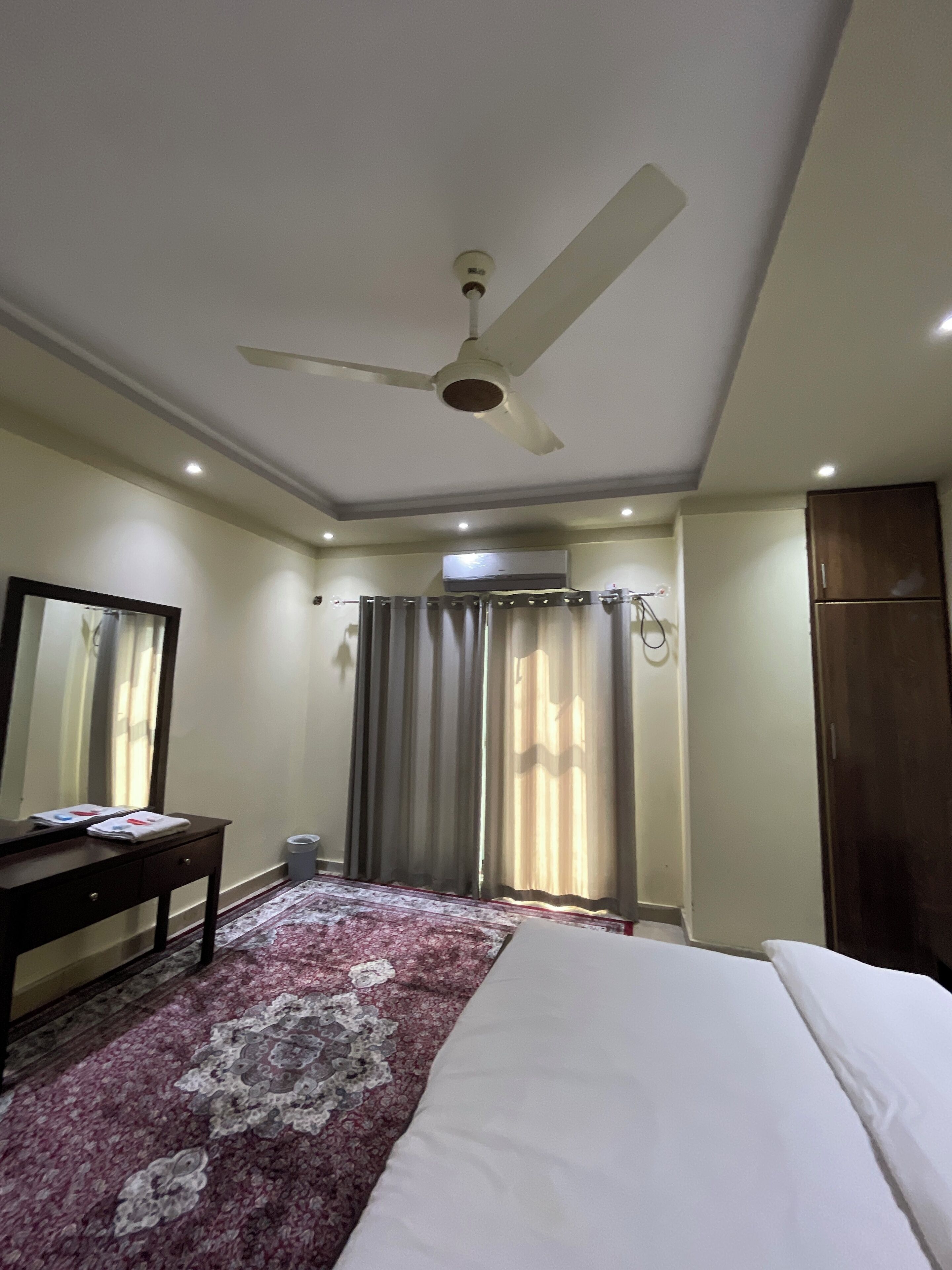 Une chambre d’hôtel équipée d’un lit, d’un bureau, d’un ventilateur de plafond, d’un appareil de climatisation et d’une fenêtre avec des rideaux.