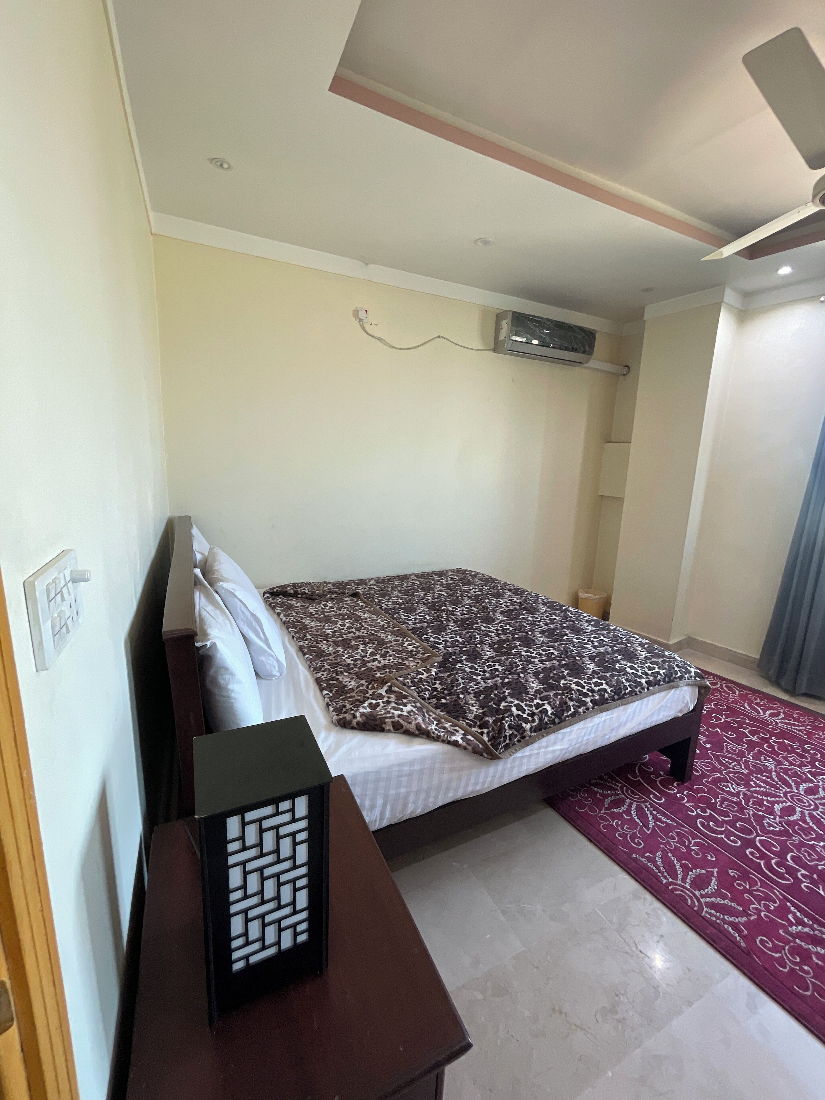 Een slaapkamer met een bed, een bureau, een airconditioning en een kamerbreed tapijt met patroon.