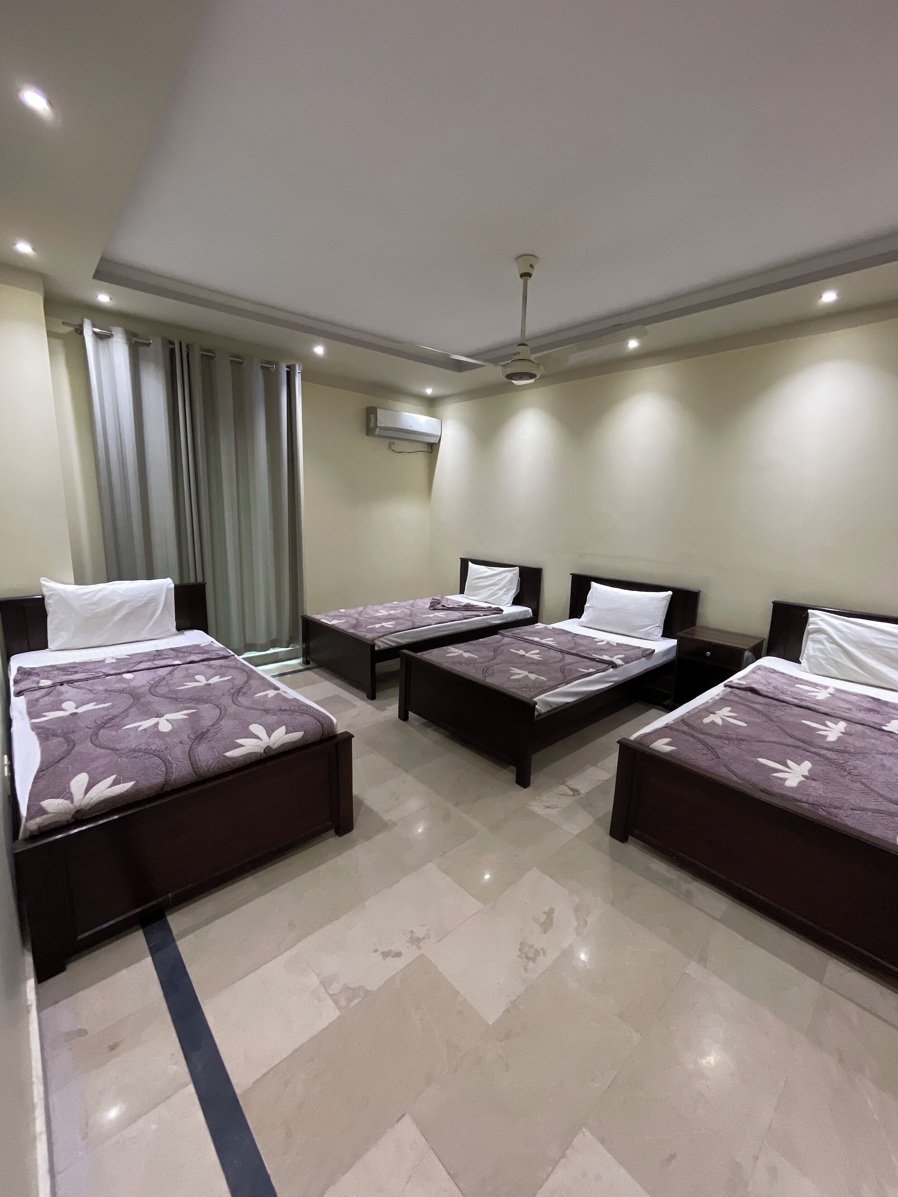 Habitación de hotel con cuatro camas, ventilador de techo, equipo de aire acondicionado y una ventana con cortinas.