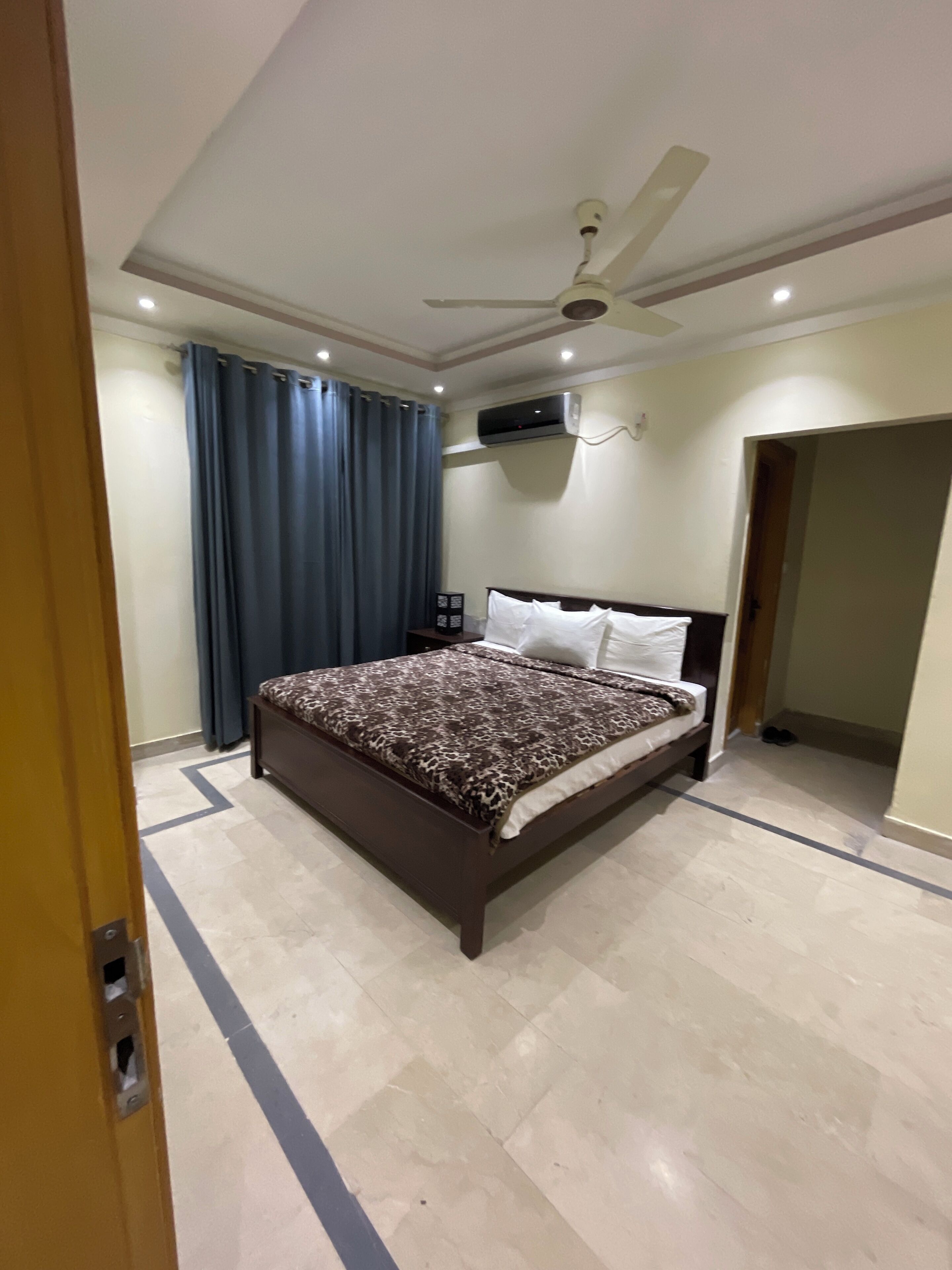 A bedroom with a bed, a ceiling fan, an air conditioning unit, a door, and a tiled floor.