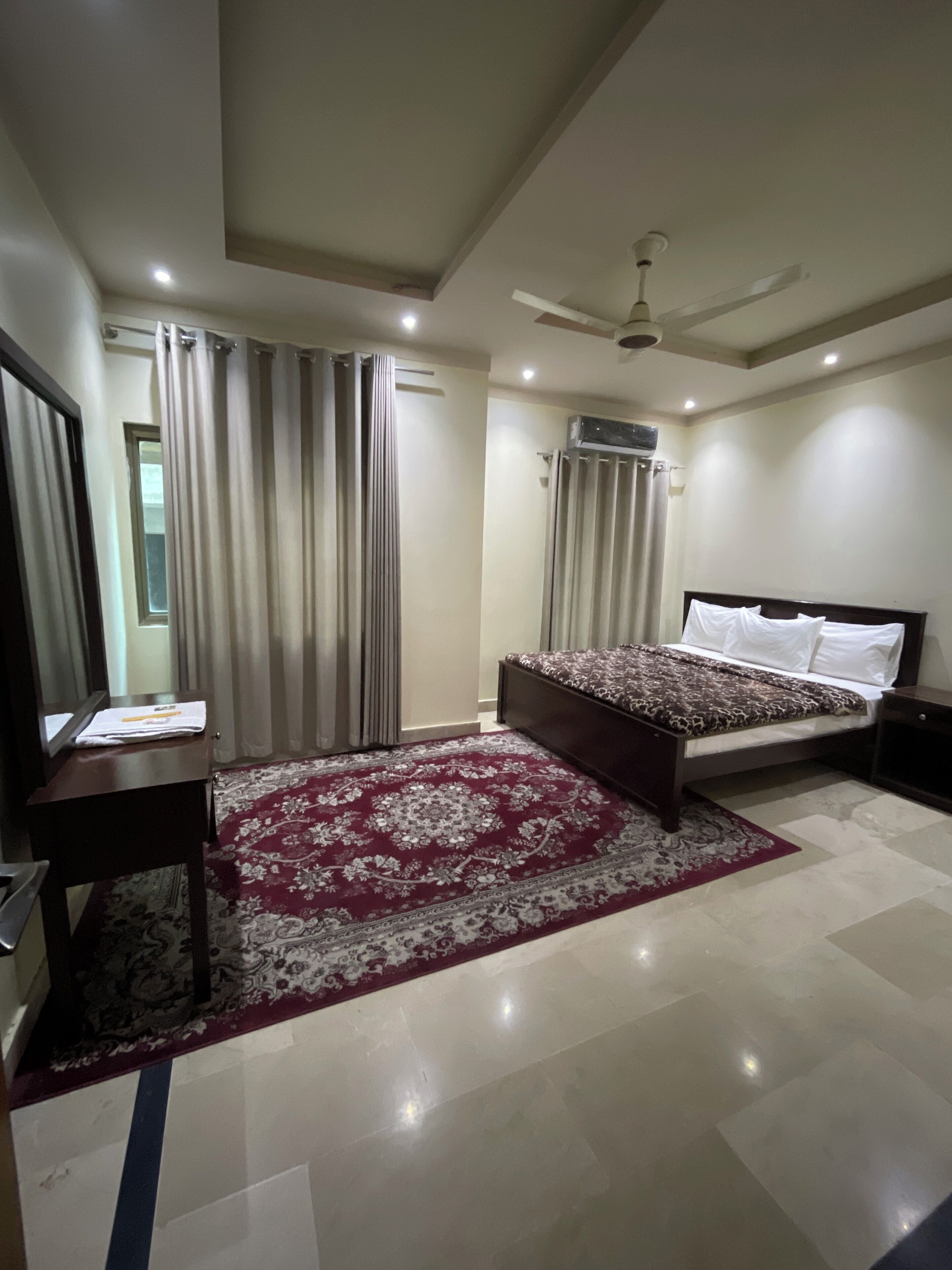 A modern bedroom with a large bed, a desk, and a ceiling fan.