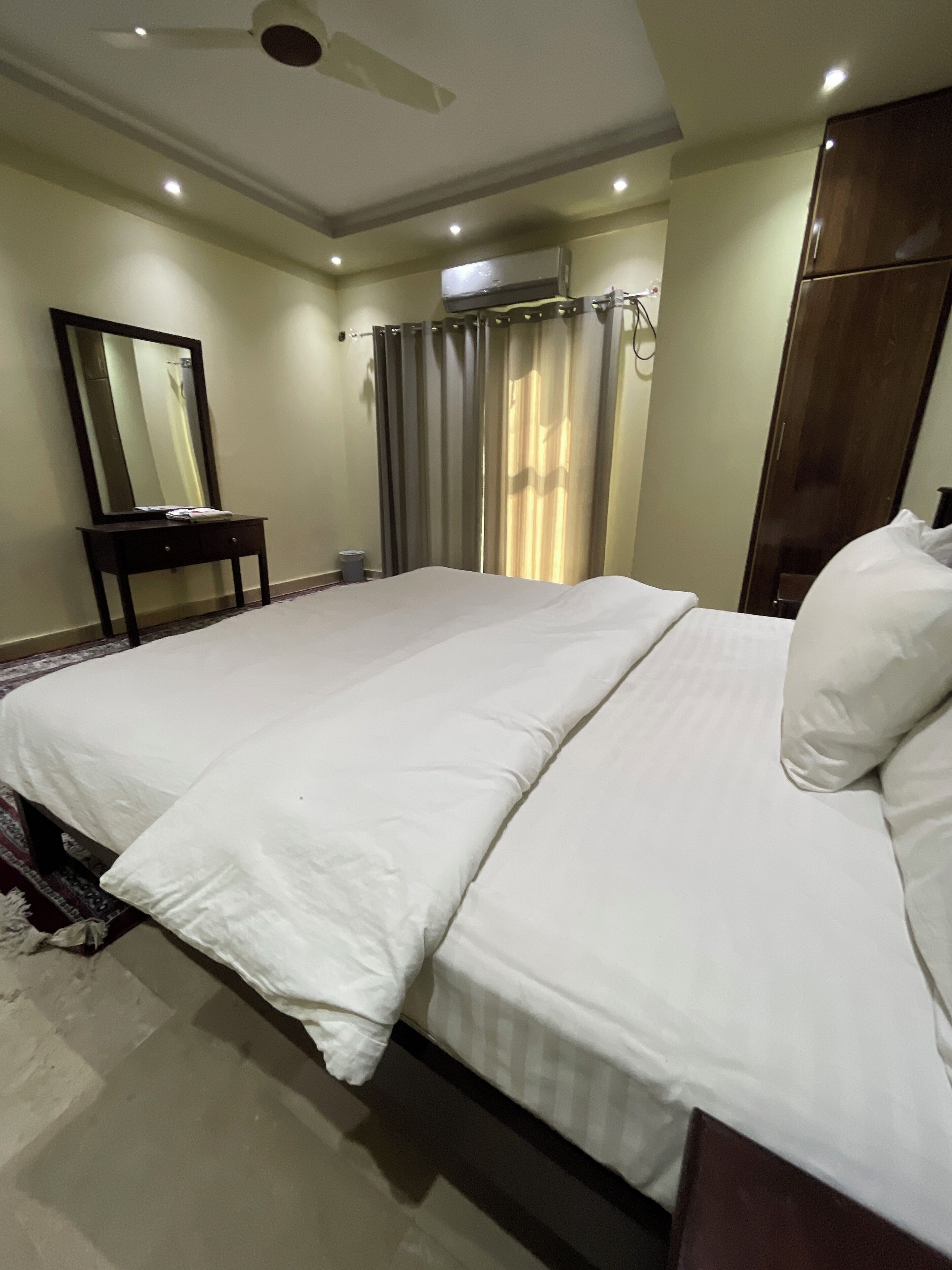 A hotel room with a large bed, a bedside table, a mirror, a wardrobe, and a ceiling fan.