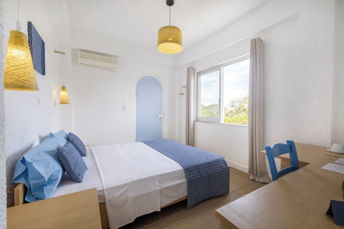 A room with a bed, a desk, a chair, a window with curtains, and a hanging light fixture.
