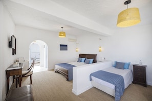 A hotel room with two beds, a desk, and a chair. There is a large window and a door leading outside. - Lassion Hotel (Sitia)