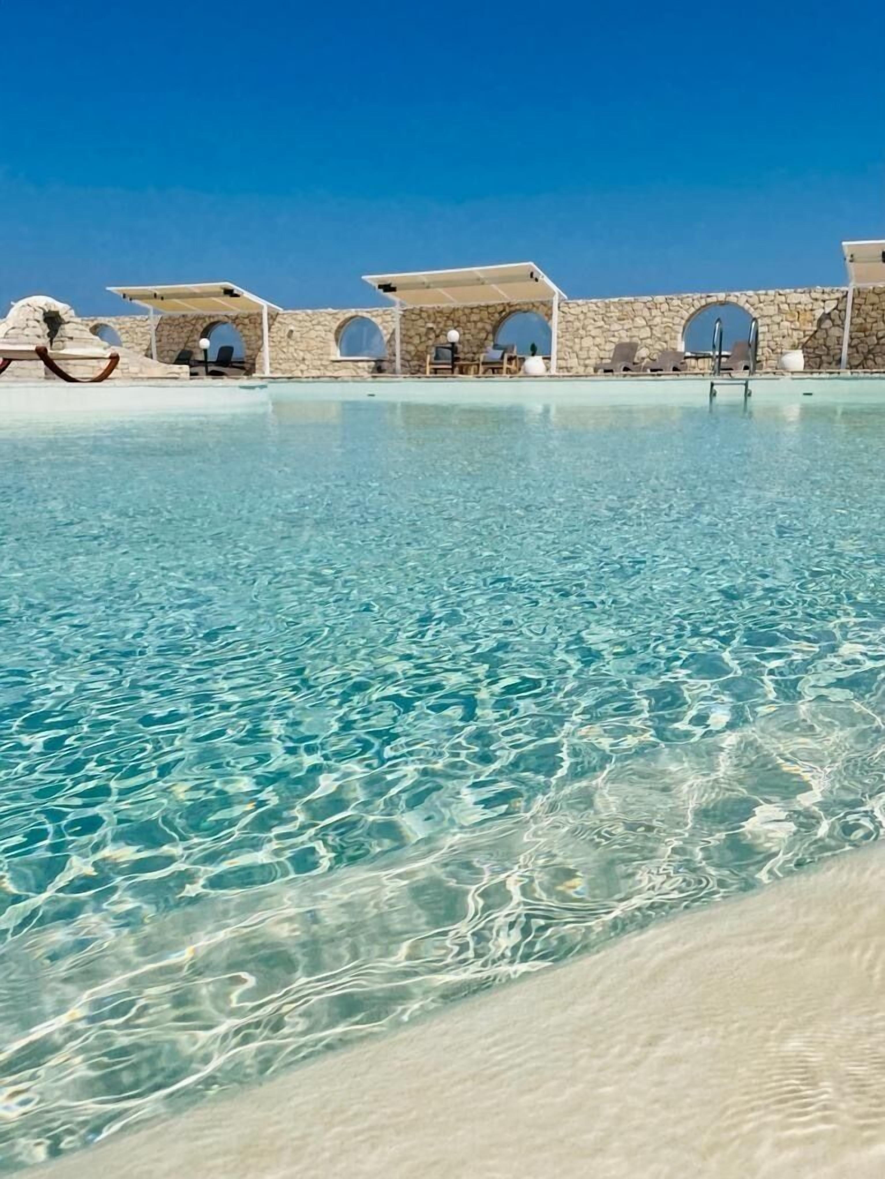 Piscina límpida com arquitetura de pedra e arcadas.