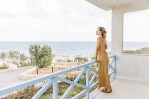 A person standing on a balcony with a view of the sea and a white structure in the background. - Lassion Hotel (Sitia)