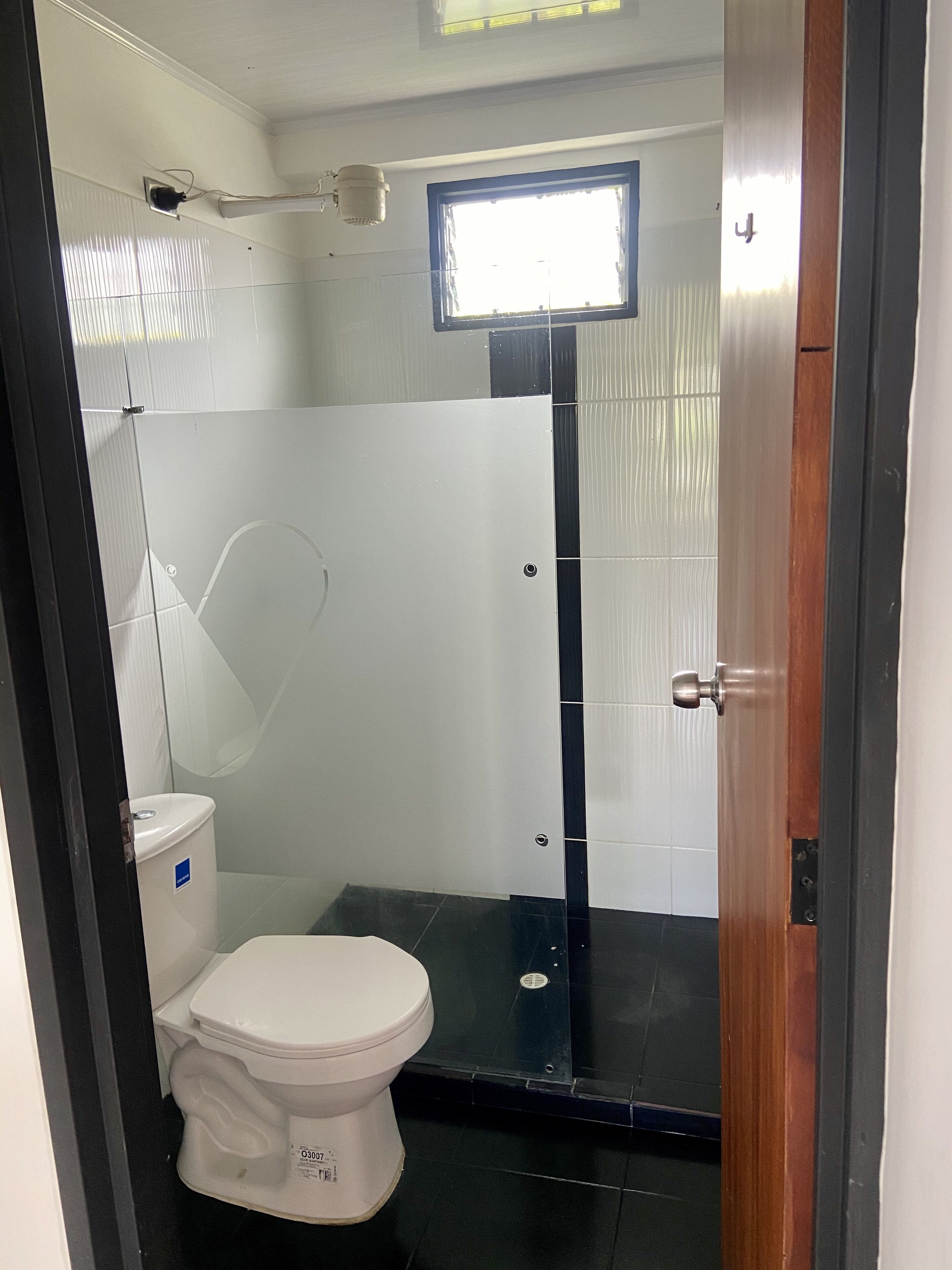 Een compacte badkamer met een wit toilet, een douchecabine van glas en een klein raam boven de douche.