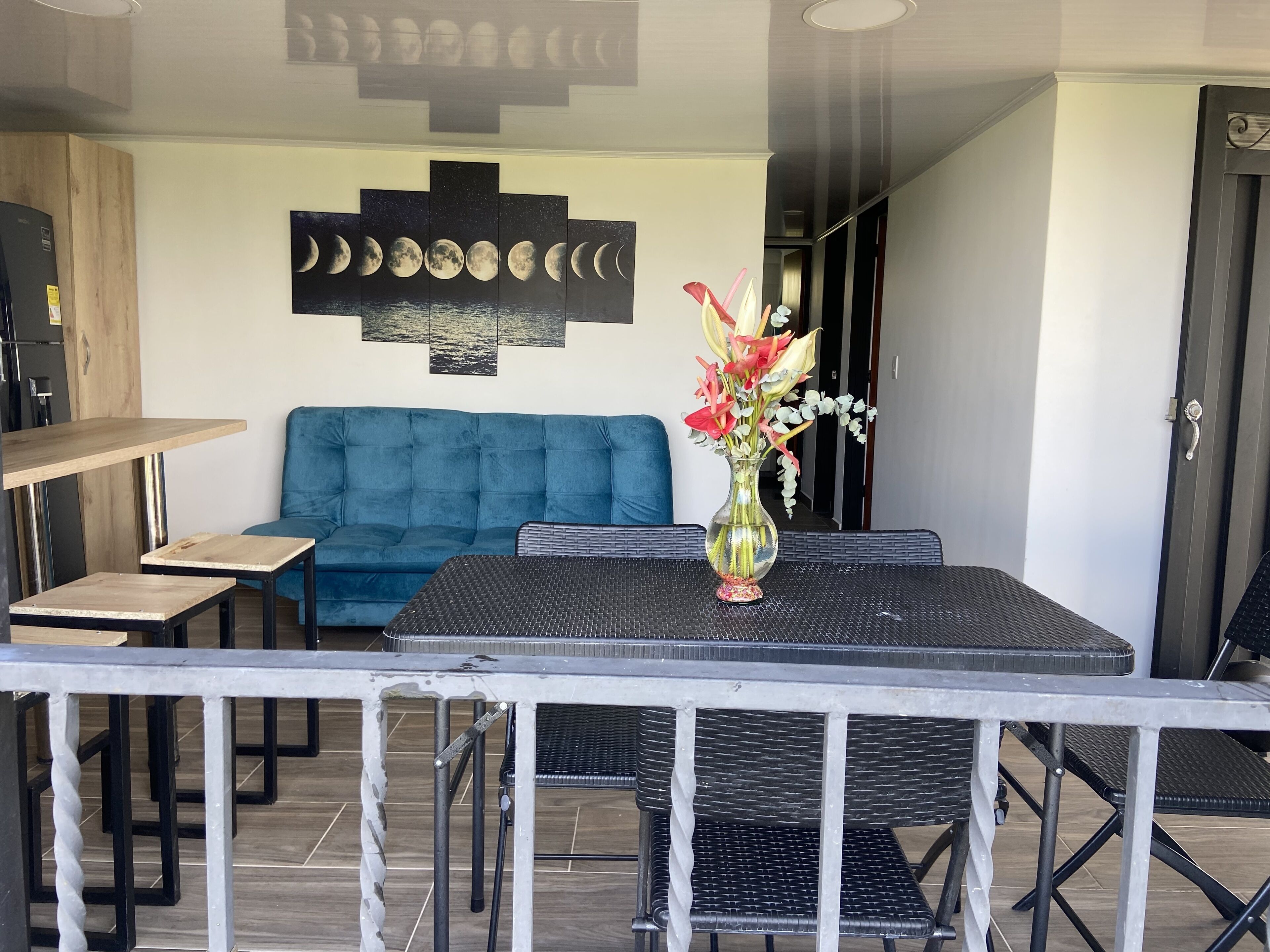 A dining area with a blue sofa, a table with a vase of flowers, and a wall with a moon phases artwork.