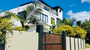 A modern two-story house with a large wooden gate, surrounded by lush greenery and palm trees. - Berakah Spa & Rooms (Guatapé)