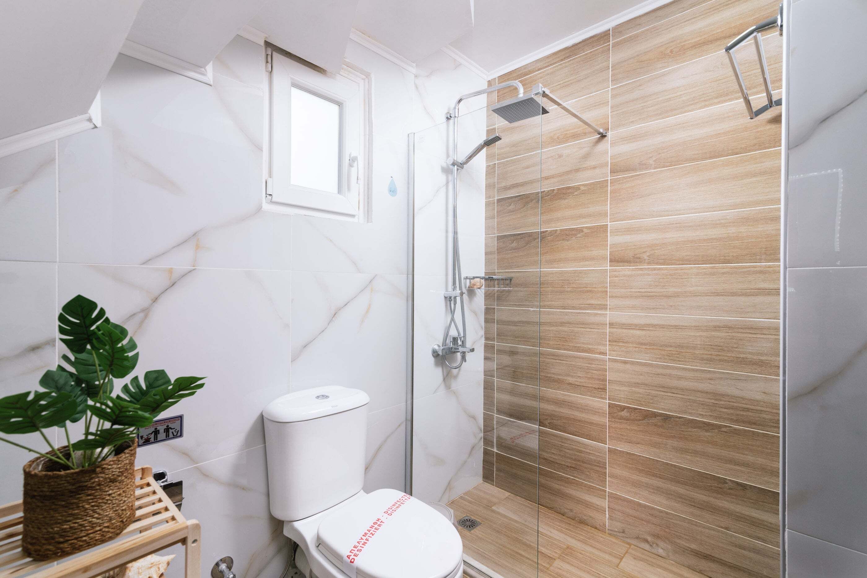 Een badkamer met een douche, toilet en een klein raam.
