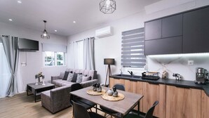 A modern living room with a sofa, a dining table, and a kitchen area with cabinets and a countertop. - ---Ammira Mare--House near sea with pool (Malevizi)
