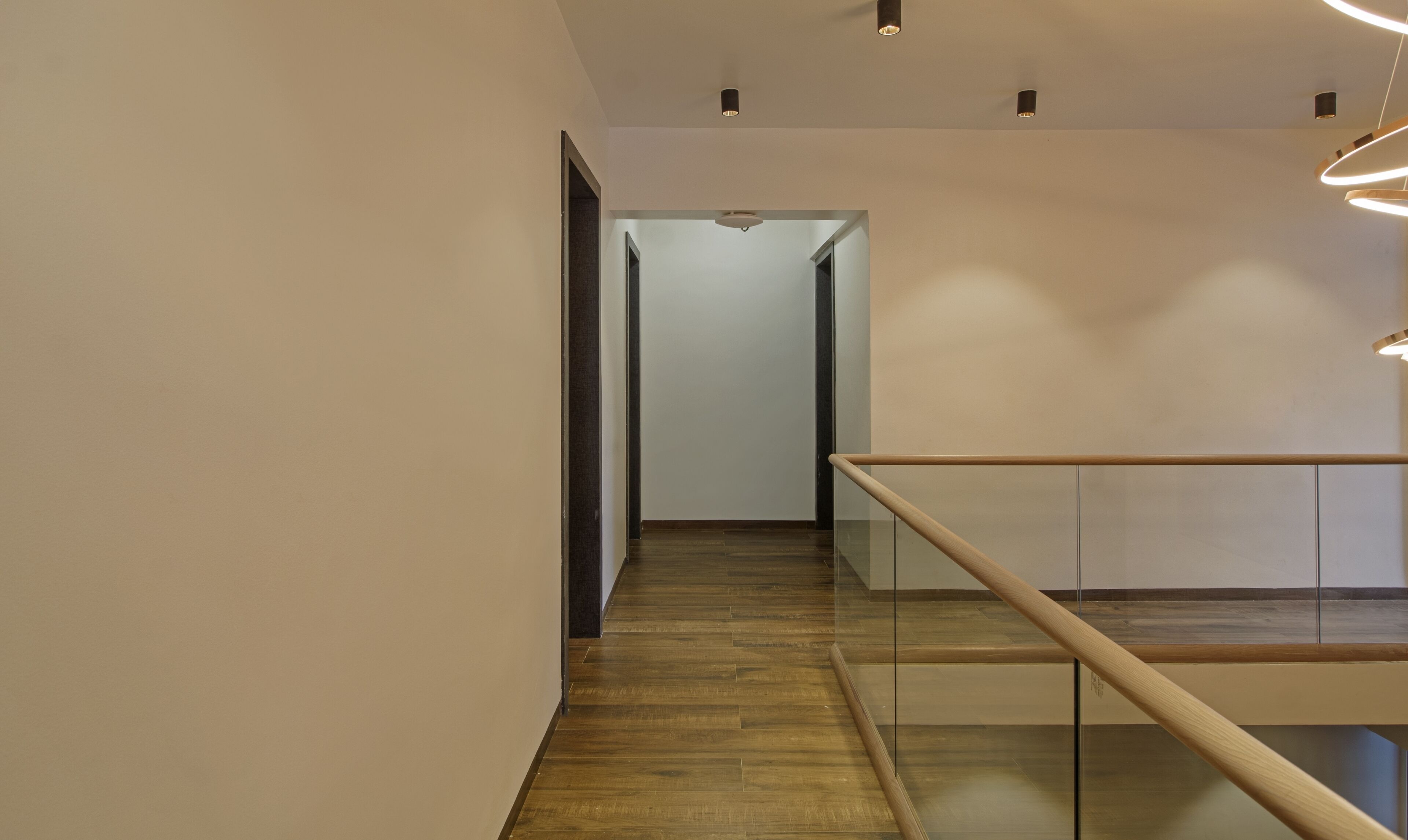Un interior moderno con suelo de madera, barandilla de cristal e iluminación empotrada.
