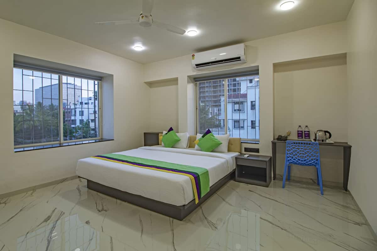 Habitación de hotel con una cama, dos ventanas, un escritorio con silla, unidad de aire acondicionado y ventilador de techo.