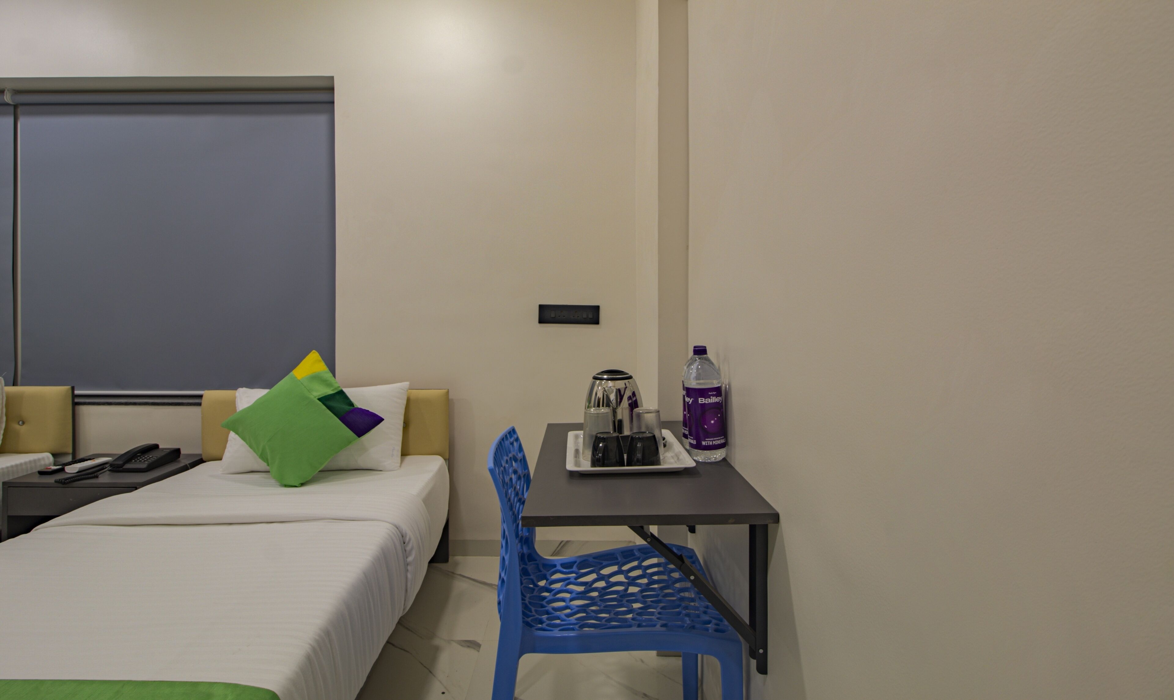 Una habitación de hotel con una cama, un escritorio con una silla, una botella de agua y una cafetera.
