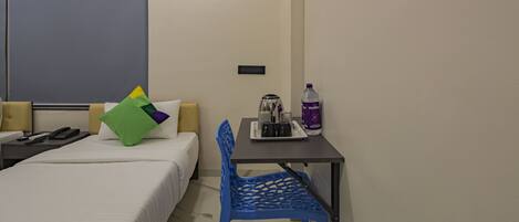 A hotel room with a bed, a desk with a chair, a water bottle, and a coffee maker.