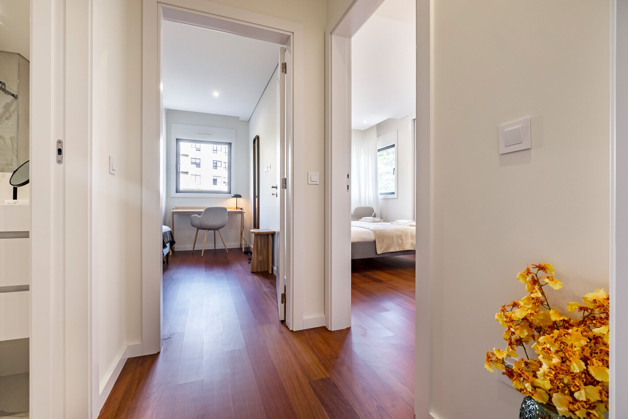 A modern apartment with a wooden floor, a dining area with a table and chairs, and a bedroom with a bed and a window.