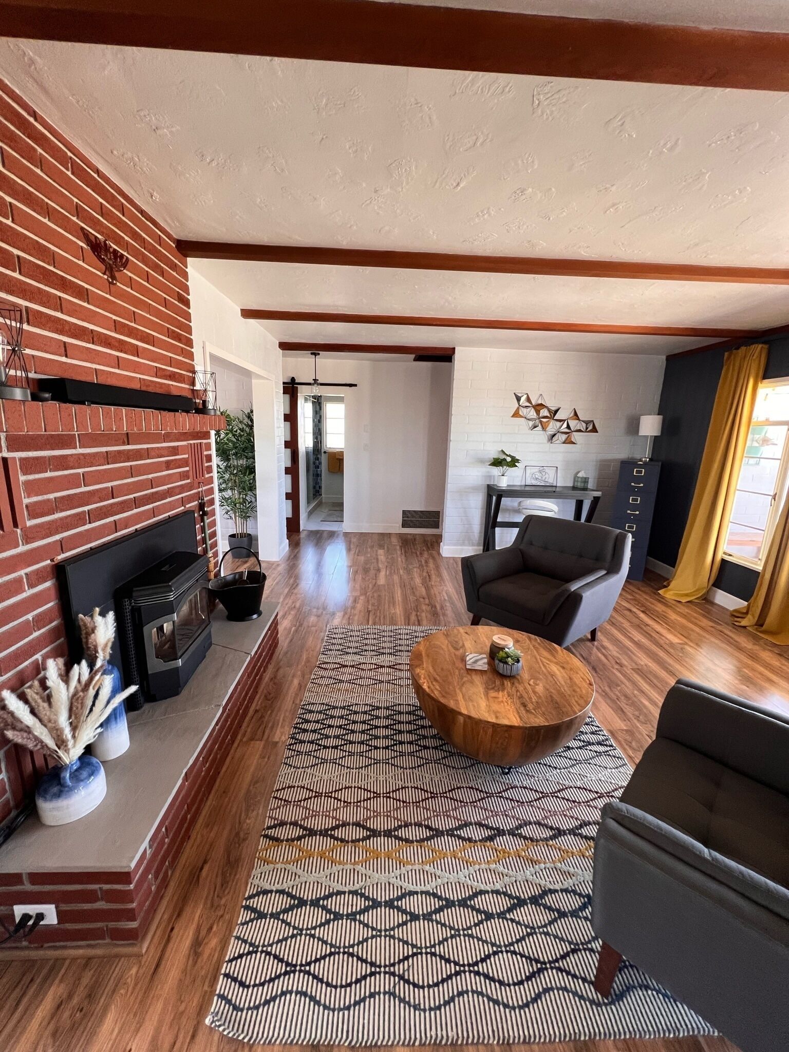 Una sala de estar moderna con una chimenea de ladrillo, una mesa de centro redonda de madera y un tapete estampado.