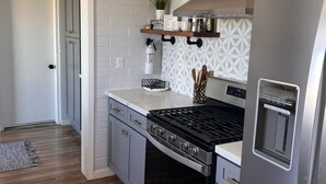 A modern kitchen with grey cabinets, a stainless steel refrigerator, a built-in stove, and a patterned backsplash.