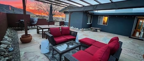 An outdoor patio with wicker furniture, a glass table, and a pergola.