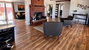 A spacious living room with a fireplace, wooden flooring, and a modern kitchen area.