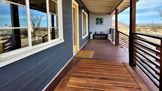 A covered porch with wooden flooring, a bench, and a view of the desert landscape.