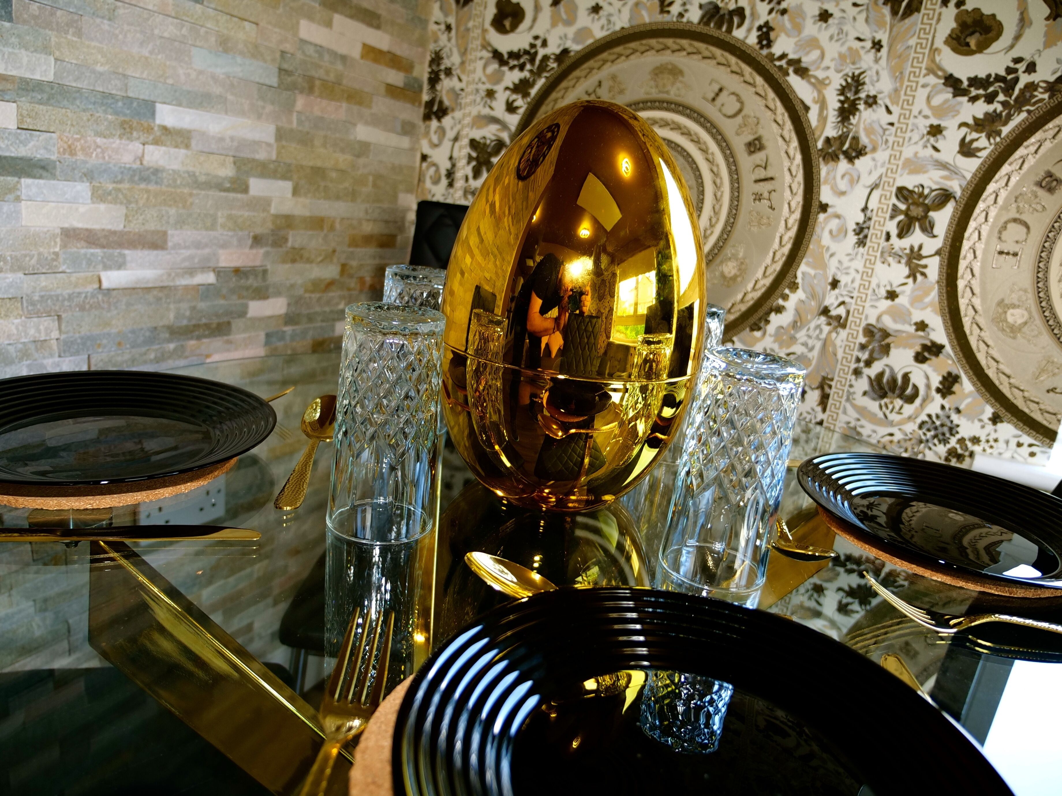 Ein Esstisch mit einer goldenen Dekoschale, klarem Glas und schwarzen Tellern.