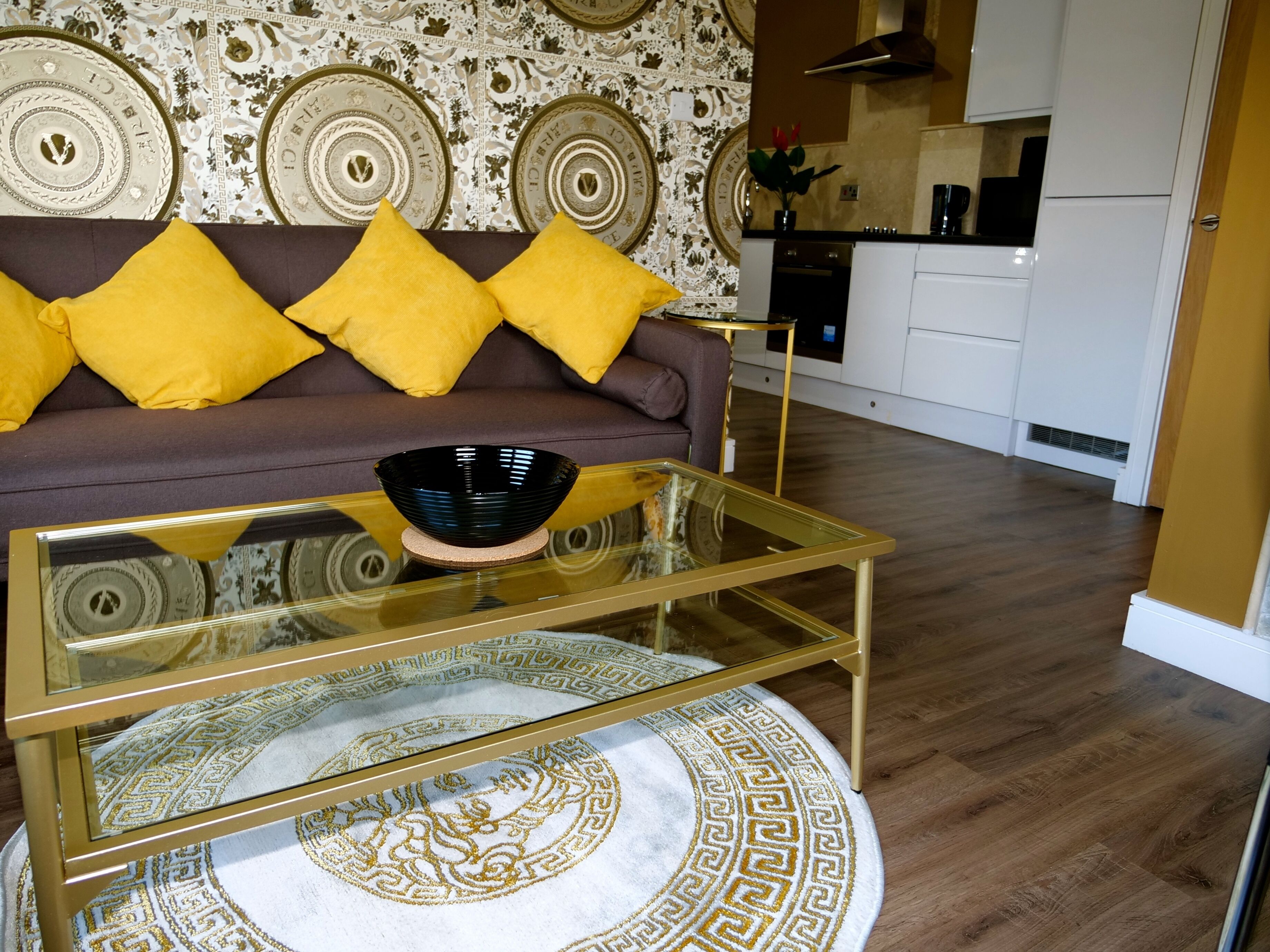 A living room with a sofa, yellow cushions, a glass coffee table, and a patterned rug.