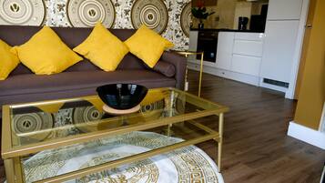 A living room with a sofa, yellow cushions, a glass coffee table, and a patterned rug.