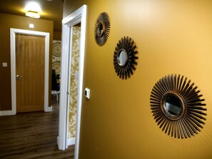 Un corridoio con una porta in legno, carta da parati decorata e tre specchi a forma di sole sulla parete.