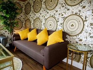 A brown sofa with four yellow cushions, a glass coffee table, and a patterned wallpaper with circular designs. - Versace Gold Apartment Opulence (South Yorkshire)